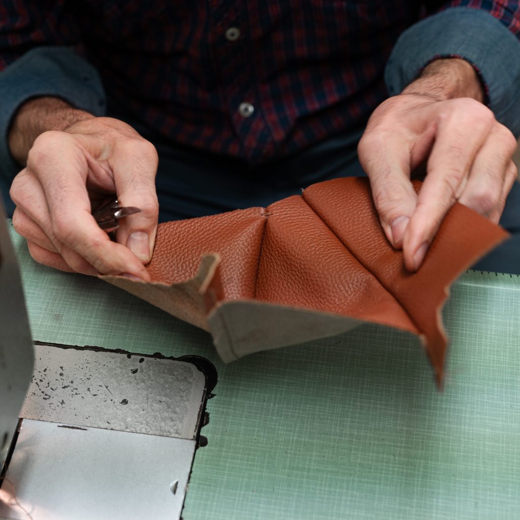 Artisan's hands folding a tan leather piece next to the sewing machine at Bojola